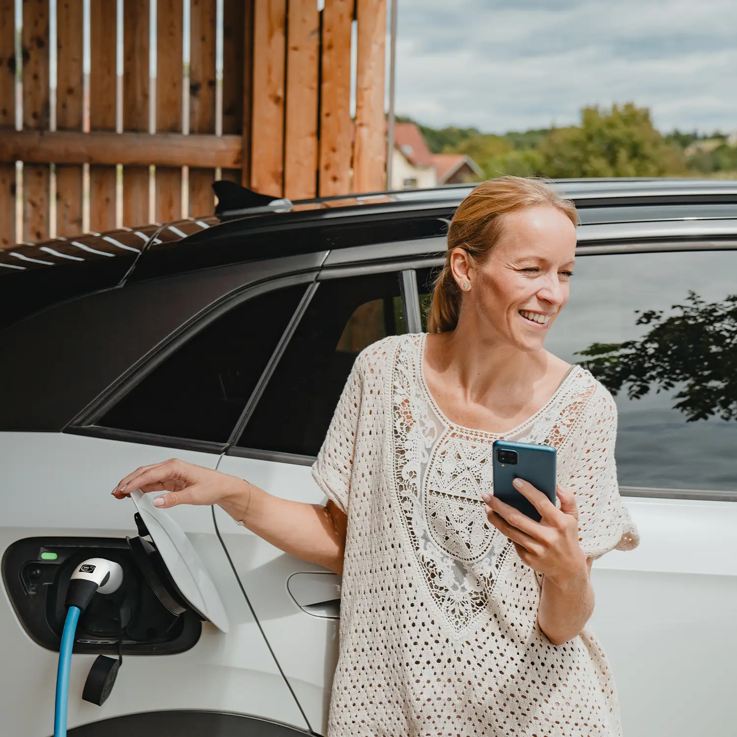 Frau nutzt Smartphone, während Elektroauto mit mobiler NRGkick-Wallbox geladen wird.
