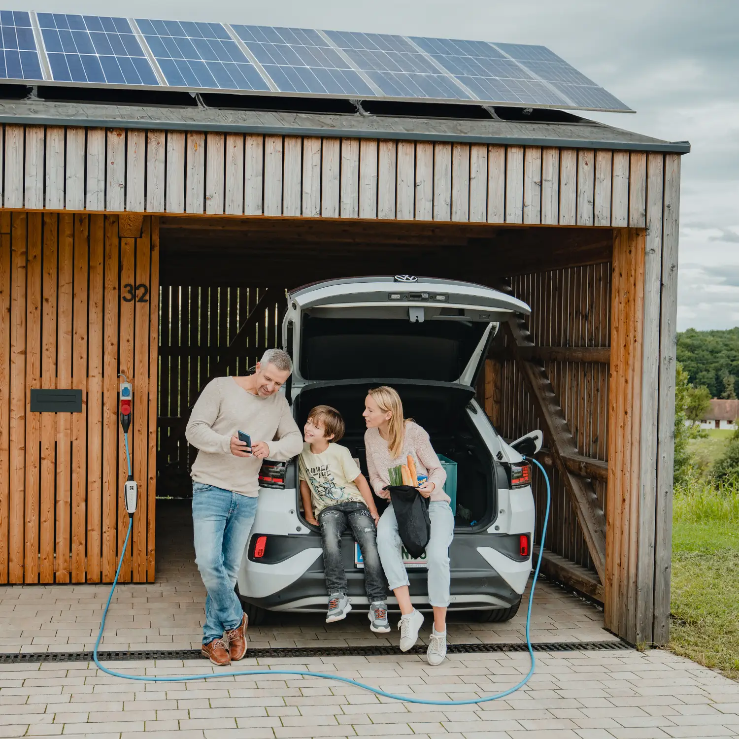 Vater zeigt Familie die NRGkick-App während Elektroauto mit NRGkick-Wallbox lädt.